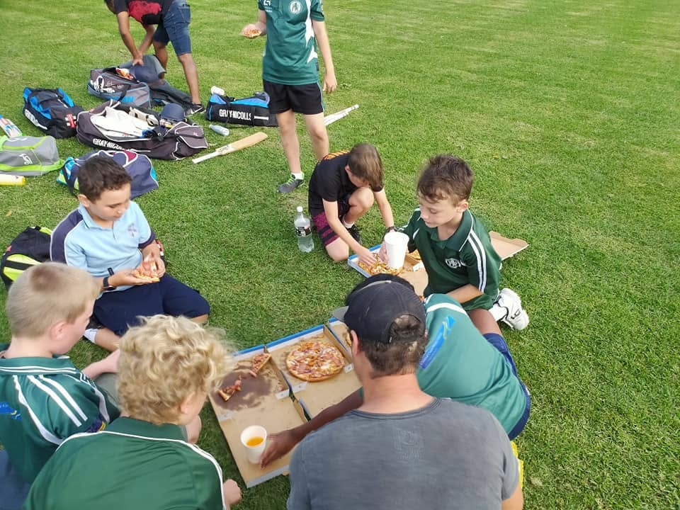 Team sharing pizzas on the grass after a game